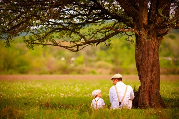 father and son sitting under the tree on spring lawn